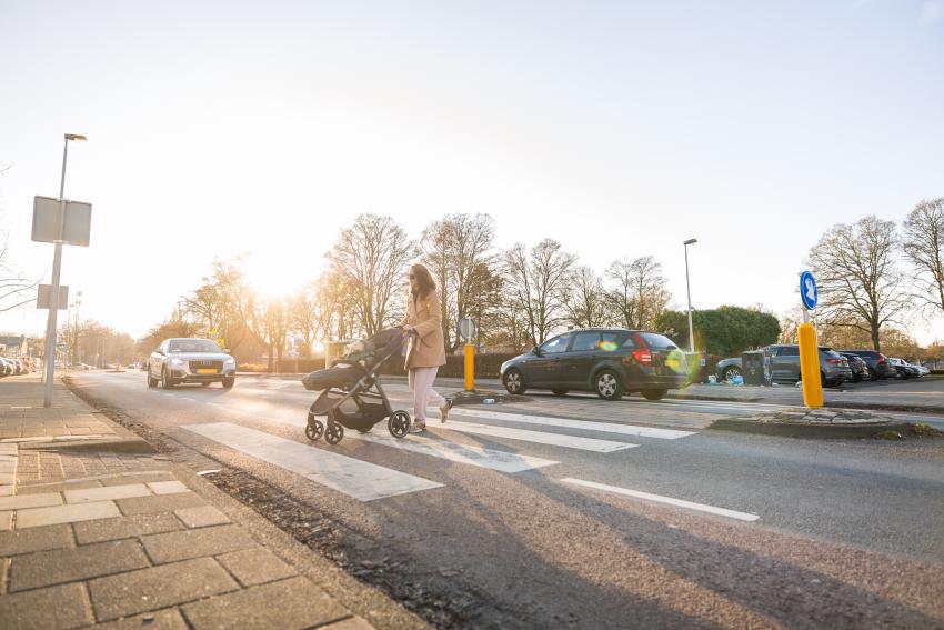 vrouw met kinderwagen steekt zebrapad over