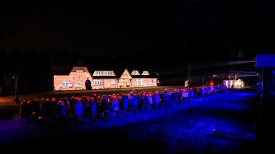 Bezoekers kijken naar een projectie op het landhuis tijdens het evenement Het Verhaal van De Wielewaal, klik voor een vergroting