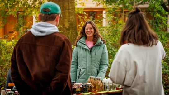 Bezoekers kijken naar een kraam met natuurproducten, klik voor een vergroting