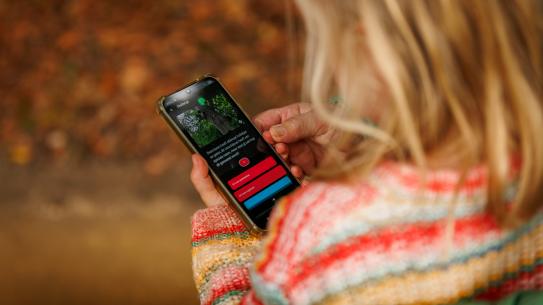 Een meisje doet een quiz over de natuur op haar telefoon, klik voor een vergroting