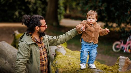 Een vader speelt met een zoon op een boomstam, klik voor een vergroting