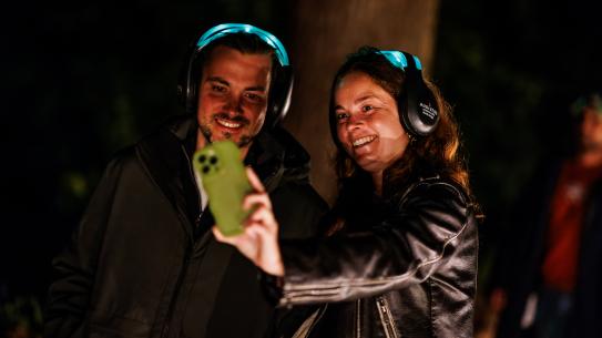 Bezoekers met een koptelefoon tijdens de openingsshow, klik voor een vergroting