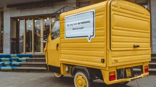 Een geel busje met daarop de tekst, 'Op weg naar de toekomst, denk je mee?', klik voor een vergroting